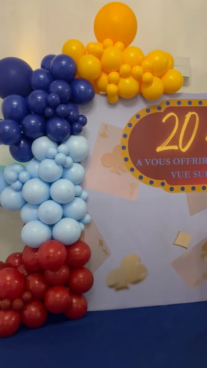 Arche de ballons bleus, jaunes et rouges autour d'un panneau « 20 ans » thème casino