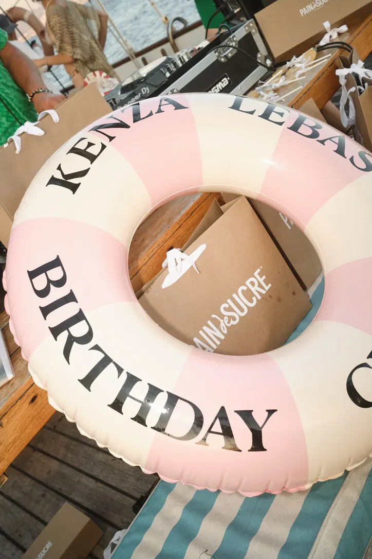 Bouée rose et blanche « Birthday » personnalisée posée sur des sacs cadeaux à bord d'un bateau