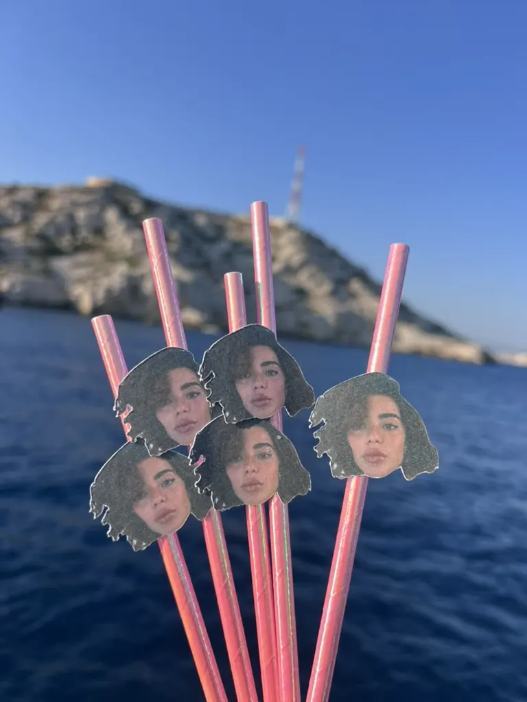 Pailles roses ornées du visage de l'invitée d'honneur devant la mer et les calanques