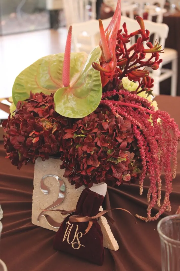 Centre de table d'hortensias bordeaux, anthuriums et amarante sur un numéro de table en pierre, mariage organisé par Kent