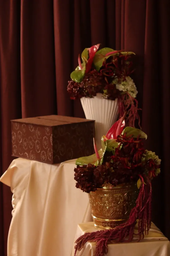 Urne à enveloppes sur drapé doré, entourée de compositions d'hortensias et d'amarante bordeaux