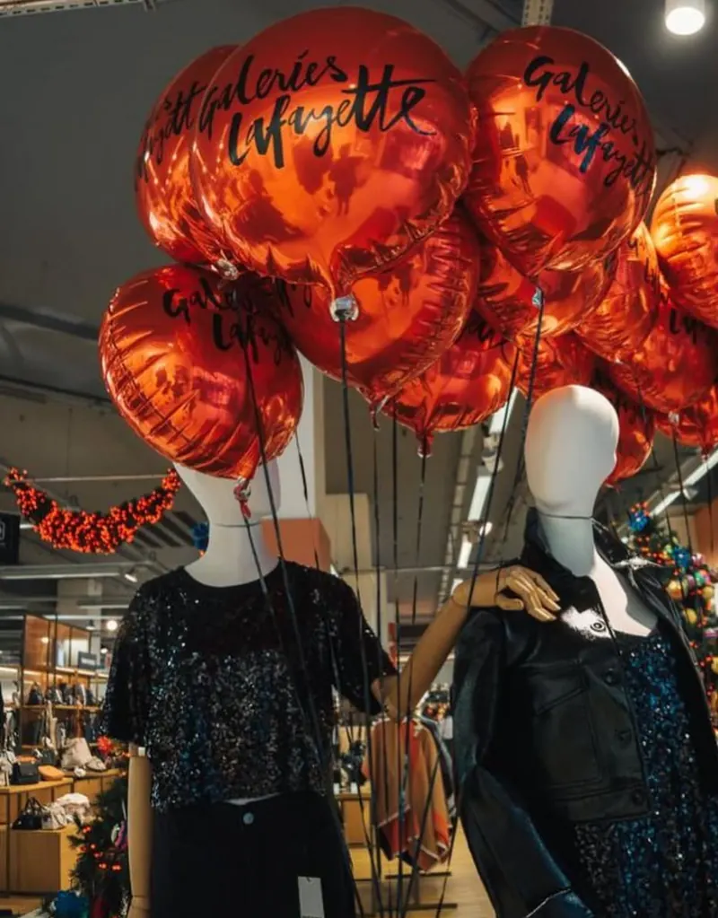 Grappe de ballons rouges « Galeries Lafayette » au-dessus de mannequins en magasin